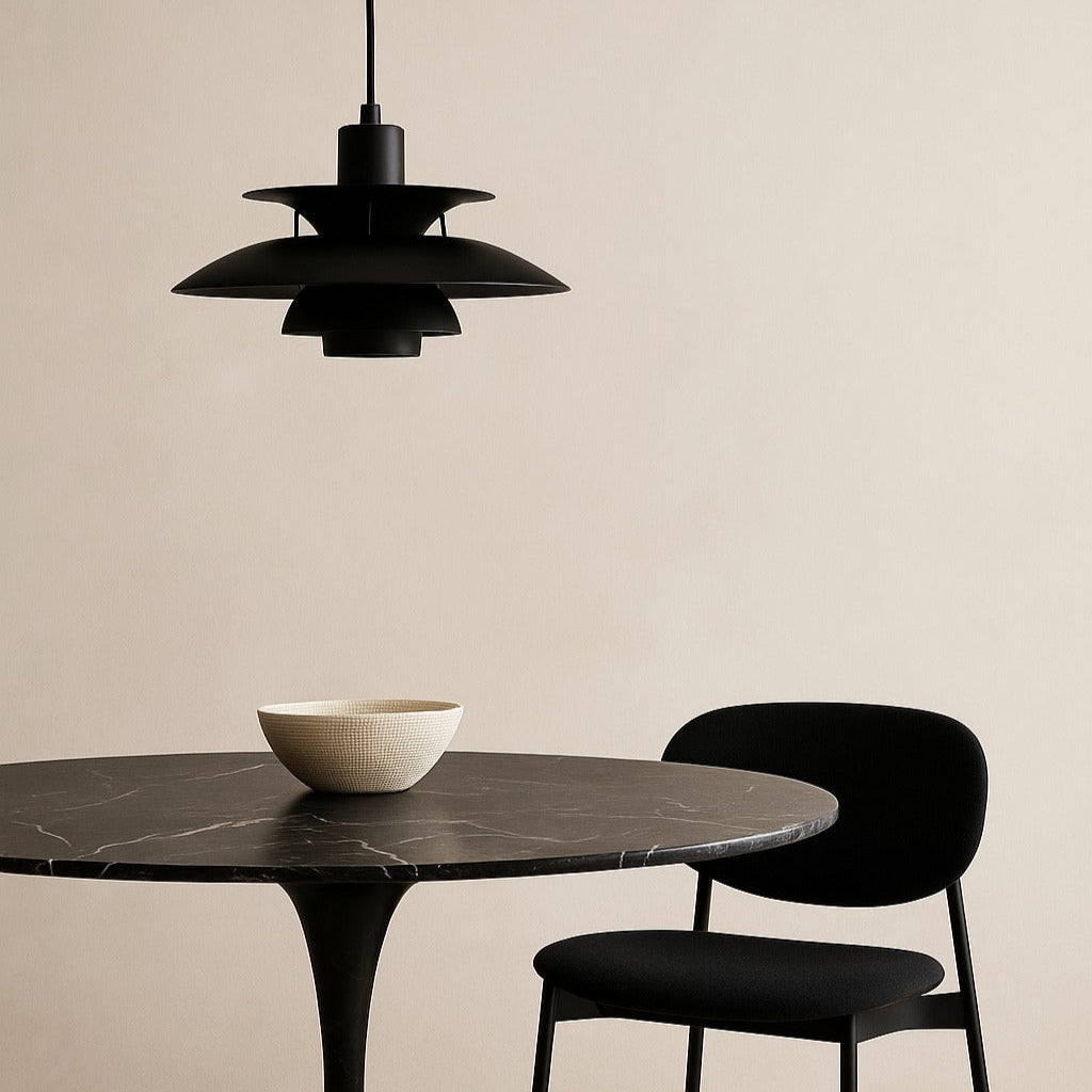 Modern dining set with black marble table and chair, and a black pendant light against a beige wall.