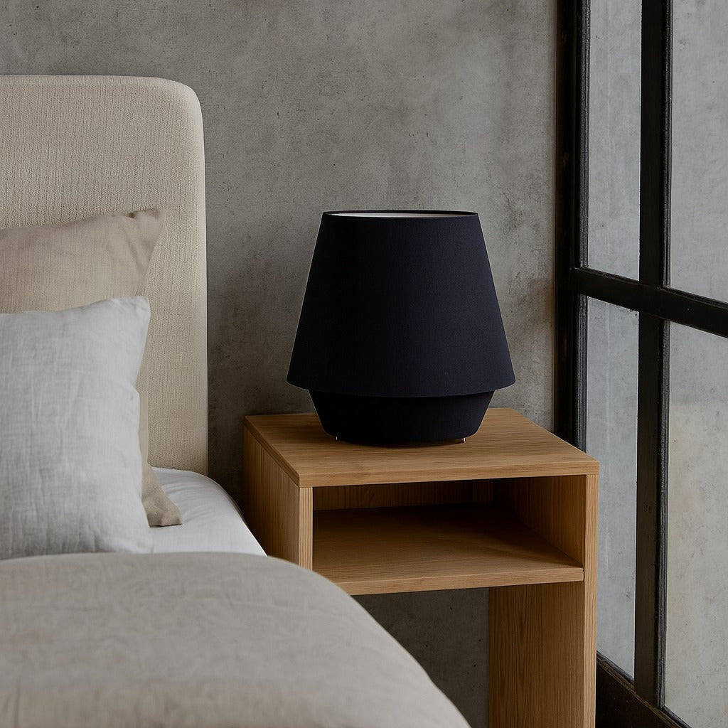 Black lamp on a wooden nightstand next to a bed with beige bedding.